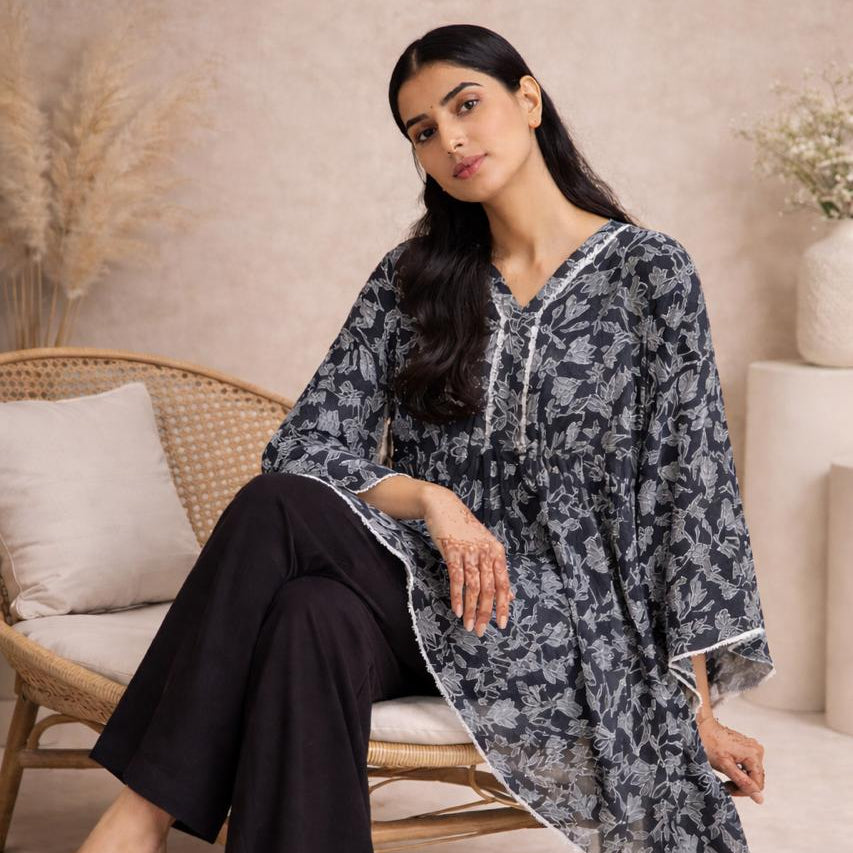 Woman sitting on a chair wearing a patterned long shirt and black pants.